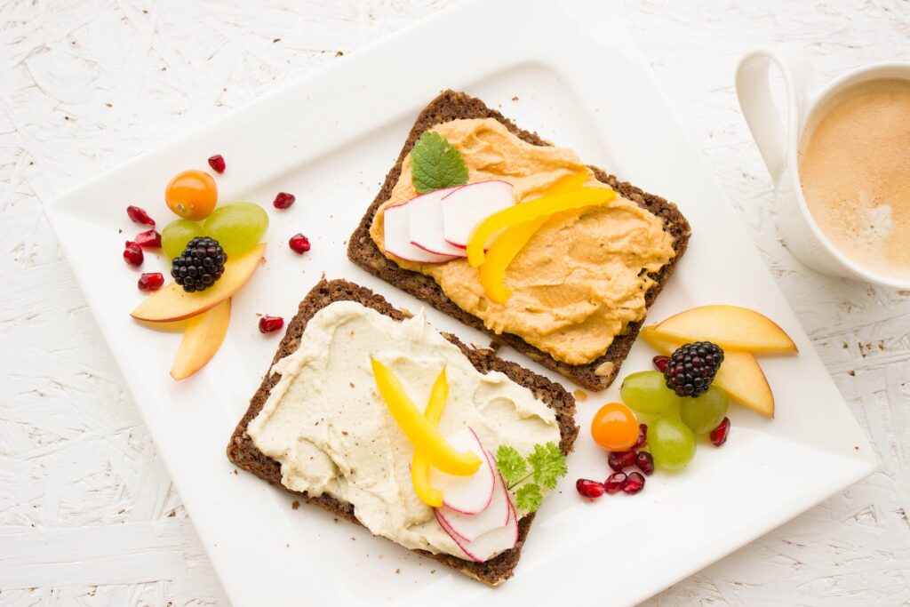 dva krajíce chleba na hranatém bílém talíři, pomazánky a kousky ovoce okolo