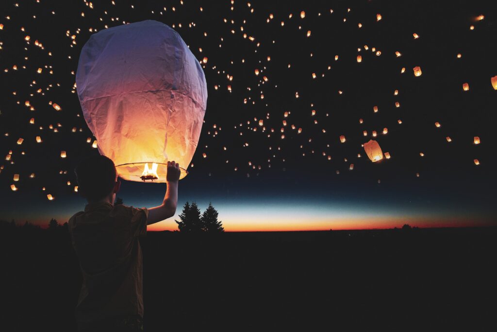 Kluk drží v ruce svítící lampion přání a v dálce na noční obloze letí stovky lampionů