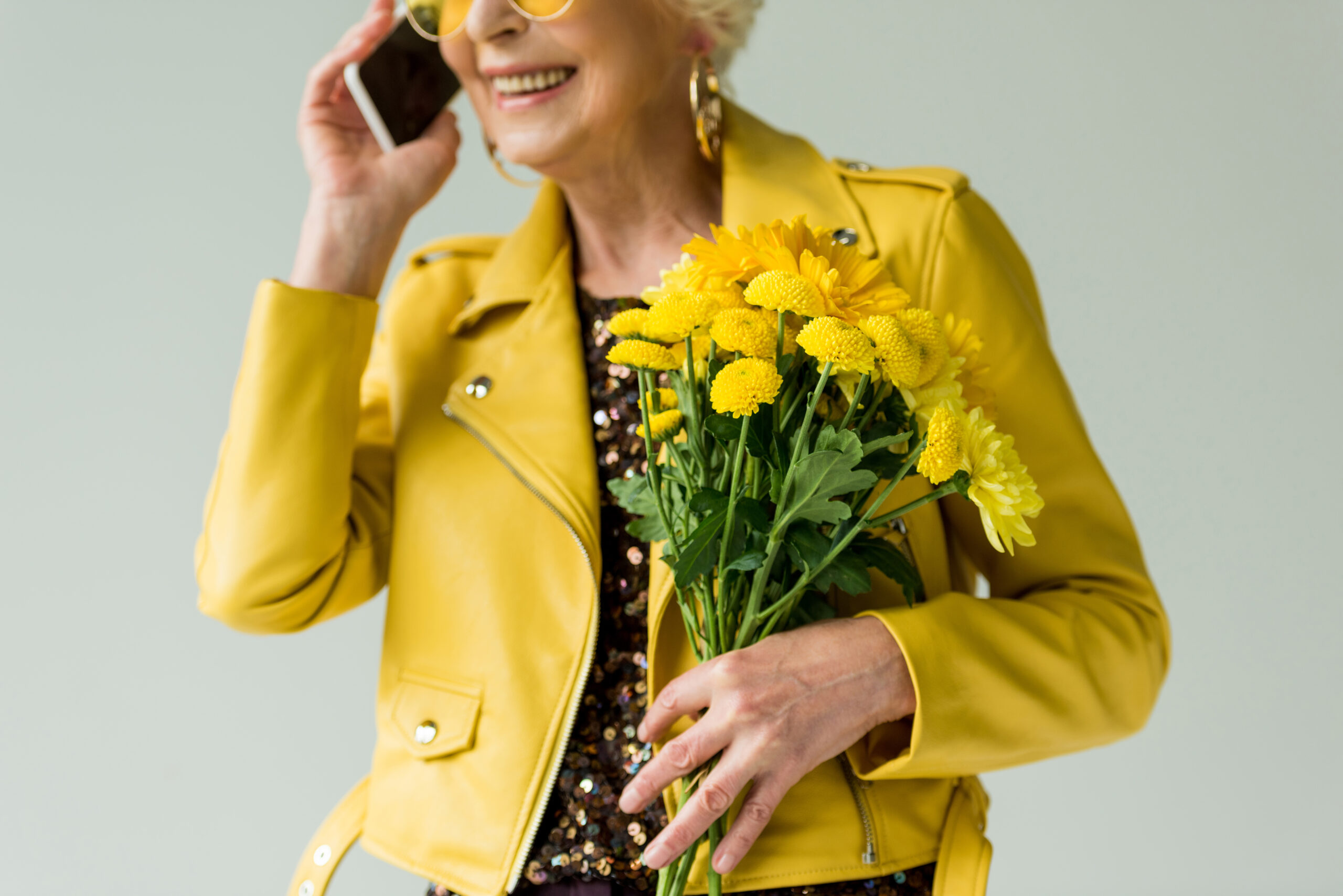 starší žena ve žluté bundě drží kytici narcisů a telefonuje